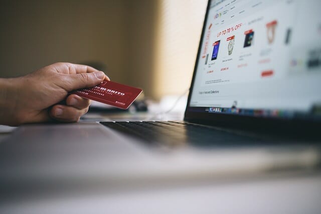 Person holding a credit card sitting at a laptop with an online shop visible on the screen, a symbolic representation of content commerce